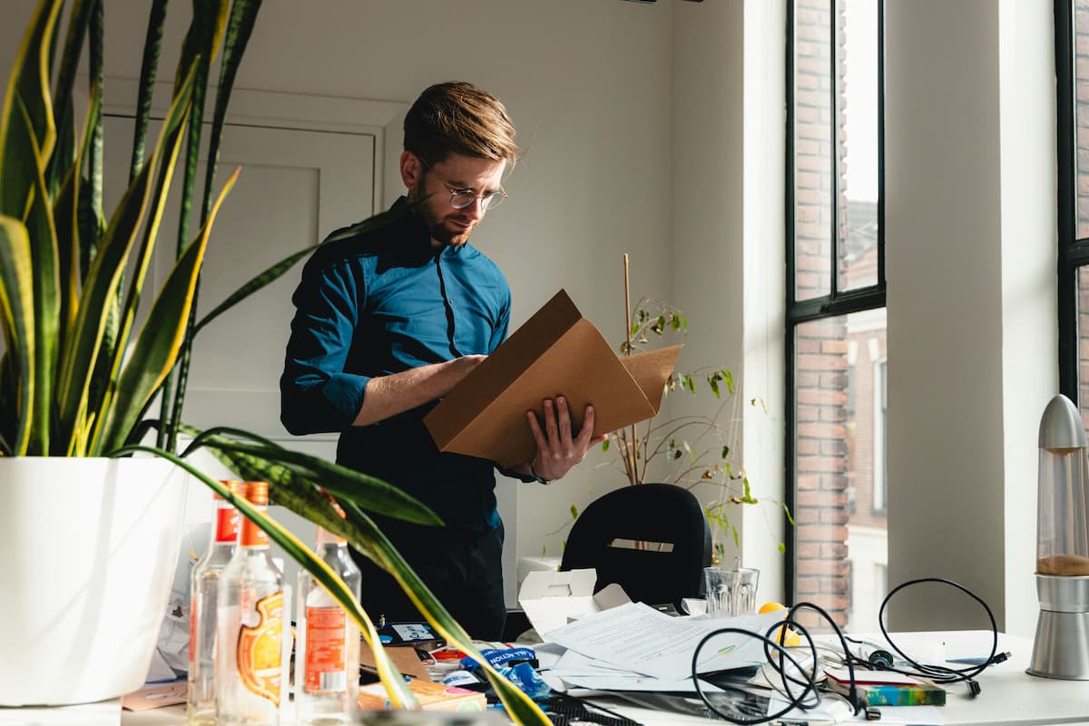 Homem, vestindo uma blusa social, está com uma posta na mão, em um ambiente que parece um home office.