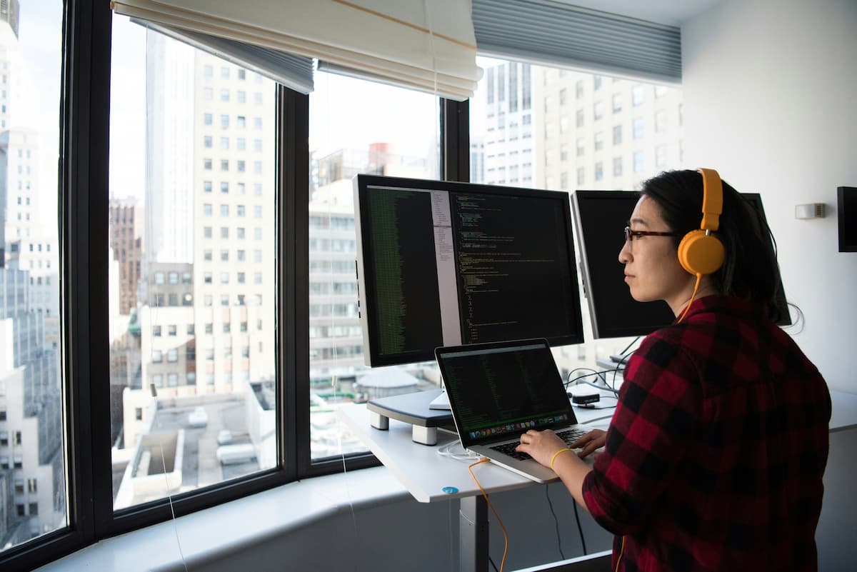 Uma mulher está sentada á frente de 4 telas de computador, desenvolvendo um software.