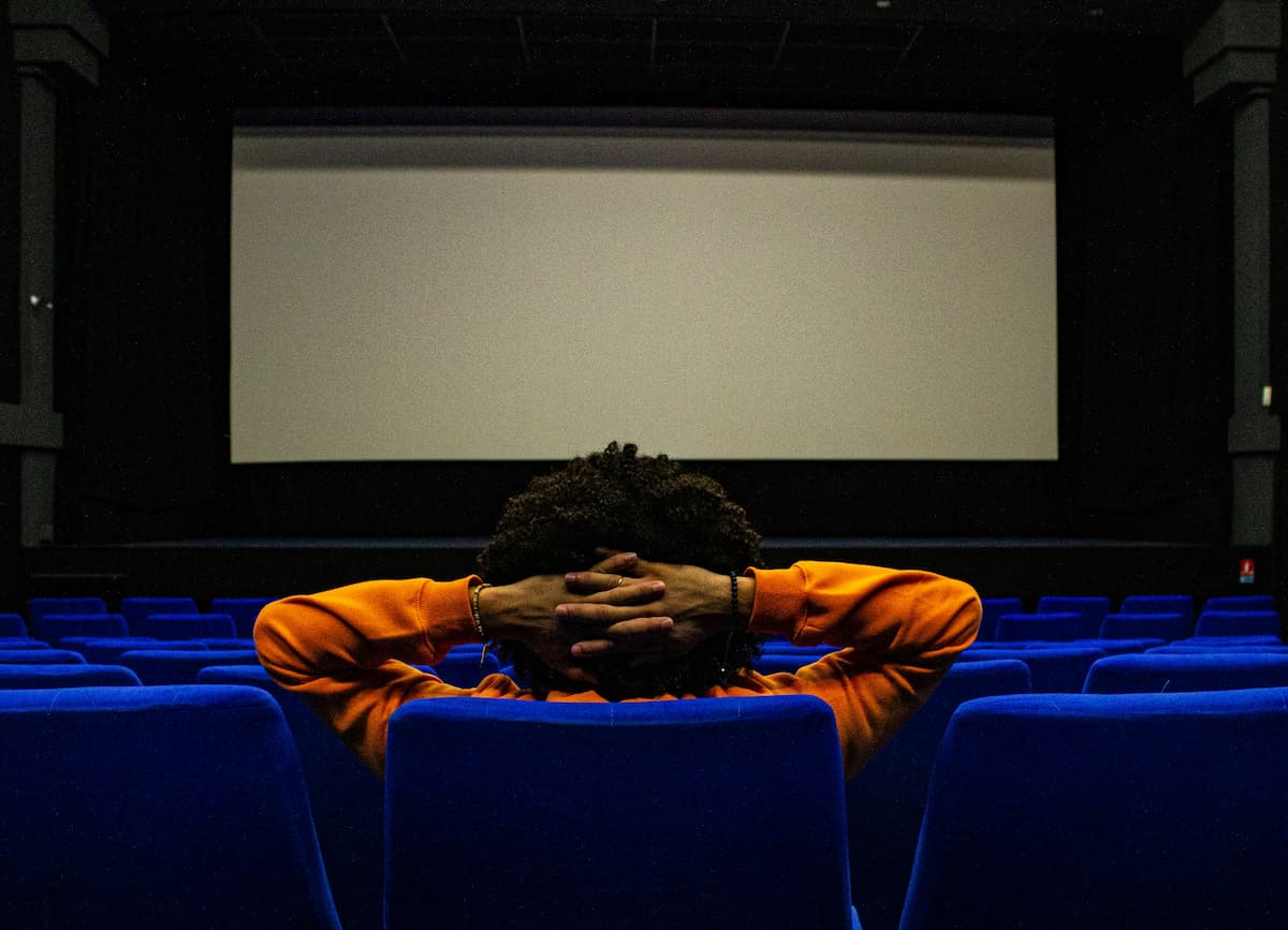 Uma pessoa de casaco laranja está esperando o início do filme na sala de cinema.